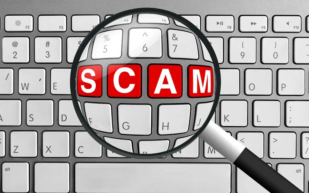 Magnifying Glass zooming on 4 red and white letters SCAM of a computer keyboard