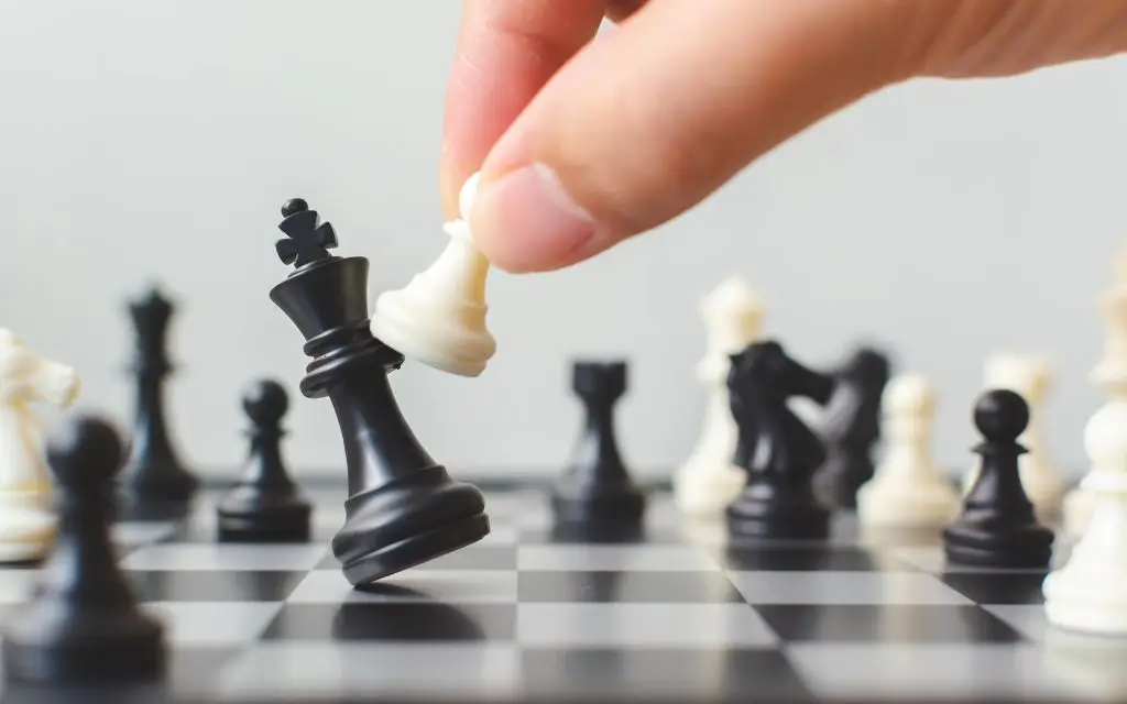 Chess Board and a hand holding a piece, kicking another piece on the black and white board illustrating what do you do after you apply for a job.