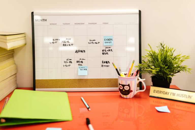 Neat workspace with a calendar, plant, and stationery on a red desk.